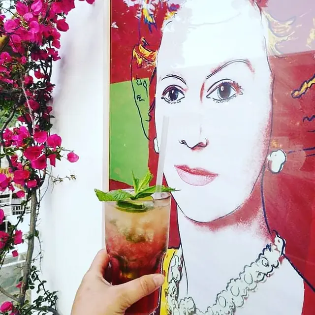A mojito held up in front of a pop-art portrait and bougainvillea