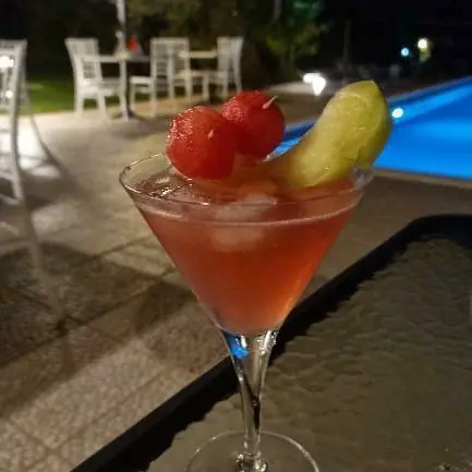 A red cocktail with watermelon beside the pool at night